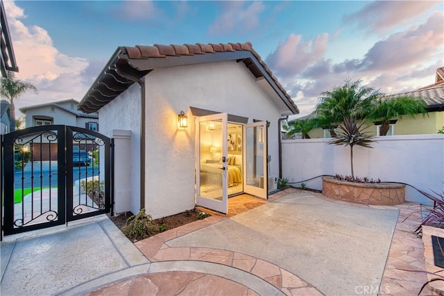 exterior space with stucco siding, a gate, a patio area, fence, and a tiled roof