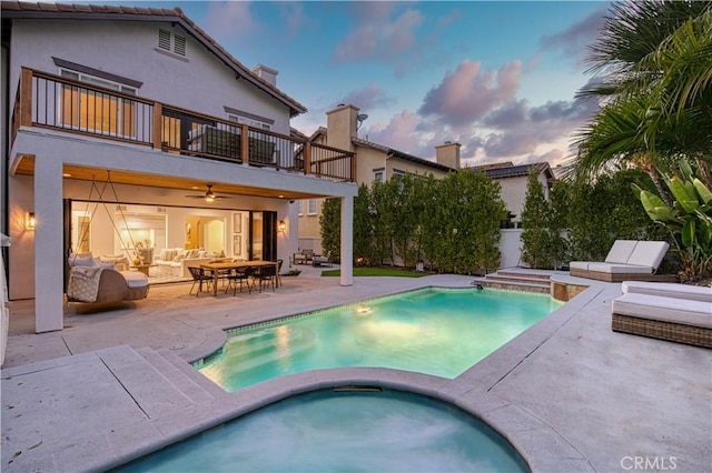 back of property at dusk featuring a fenced in pool, stucco siding, a balcony, an in ground hot tub, and a patio area
