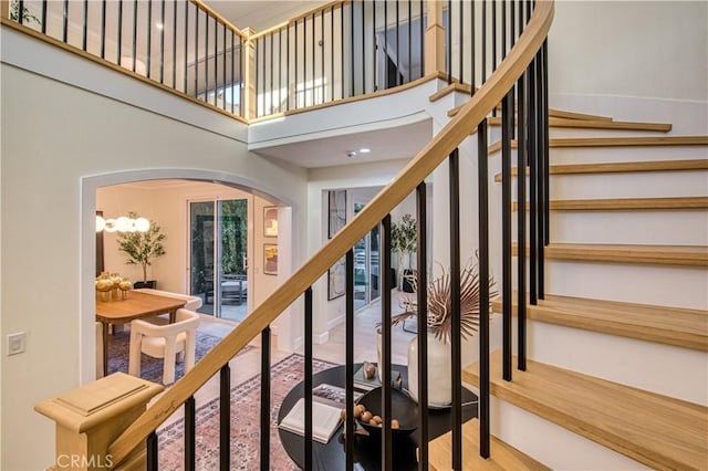 stairs featuring a chandelier, arched walkways, a towering ceiling, and wood finished floors