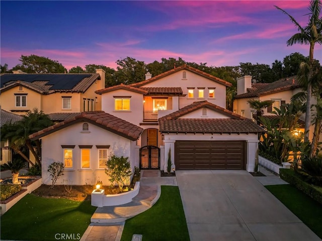 mediterranean / spanish-style house featuring stucco siding, concrete driveway, an attached garage, a gate, and a balcony