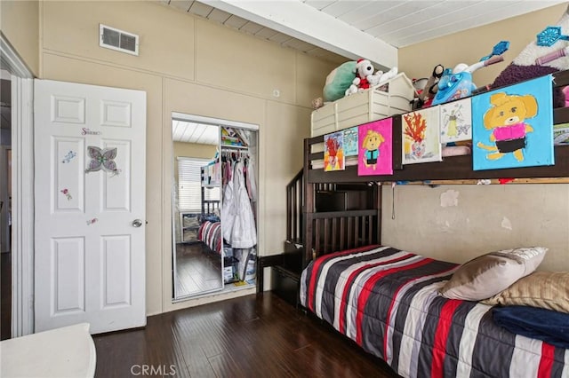 bedroom with dark wood-style floors, a closet, visible vents, and beam ceiling