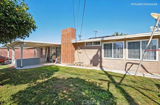 rear view of property featuring a yard, a patio, a chimney, and stucco siding