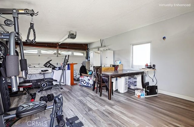 exercise area with a garage, a textured ceiling, baseboards, and wood finished floors