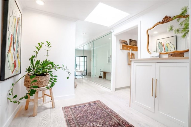 corridor featuring light wood-type flooring, a skylight, crown molding, and baseboards