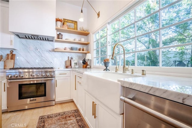 kitchen featuring stainless steel appliances, wall chimney exhaust hood, white cabinets, and light stone countertops