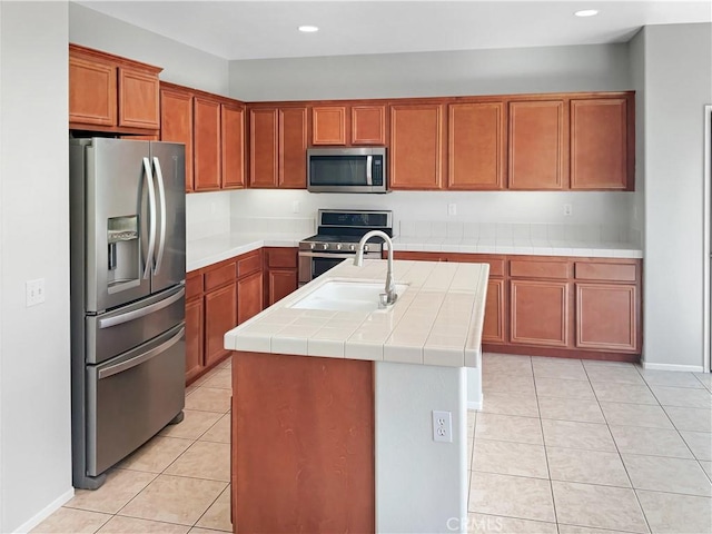 kitchen featuring a center island with sink, tile countertops, light tile patterned floors, stainless steel appliances, and a sink