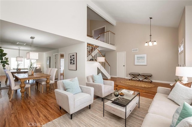 living room with visible vents, light wood-style flooring, stairway, a notable chandelier, and beam ceiling