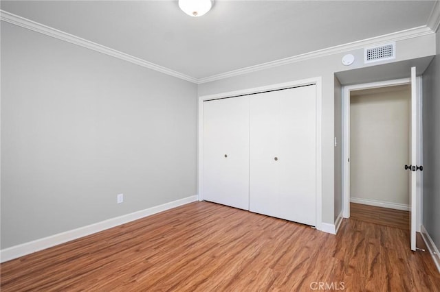 unfurnished bedroom with a closet, wood finished floors, visible vents, and crown molding