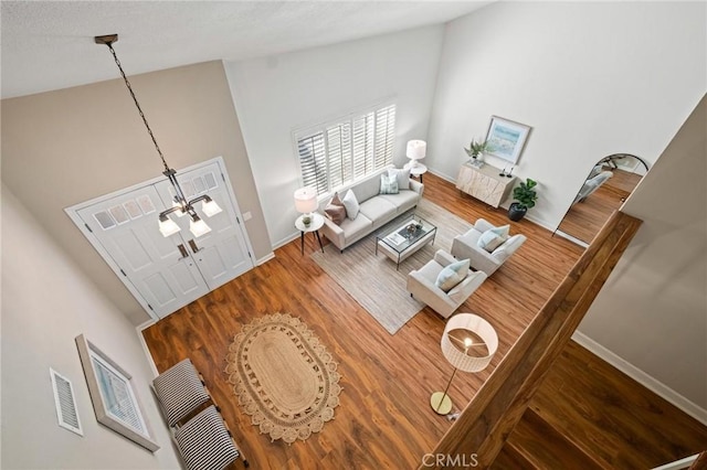 living area with high vaulted ceiling, wood finished floors, visible vents, and baseboards