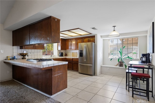 kitchen with tile countertops, stainless steel appliances, a peninsula, backsplash, and a wealth of natural light