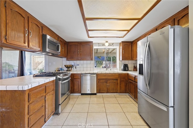 kitchen featuring appliances with stainless steel finishes, brown cabinetry, backsplash, and light tile patterned floors