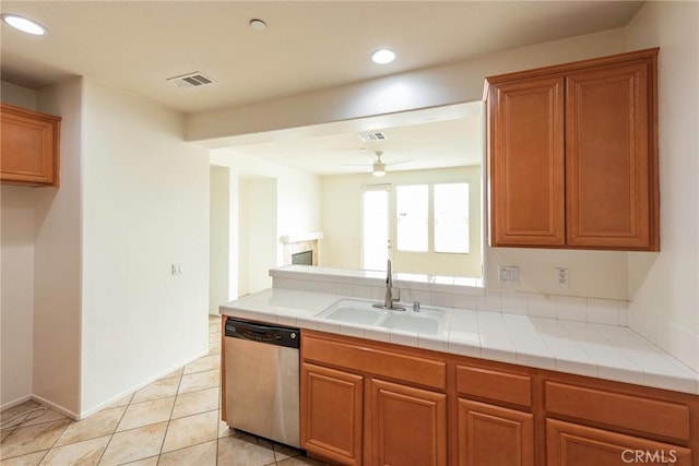 kitchen with brown cabinets, tile counters, visible vents, stainless steel dishwasher, and a sink