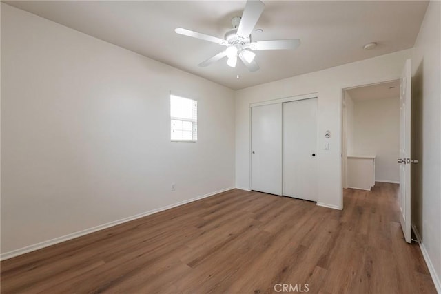 unfurnished bedroom with ceiling fan, a closet, wood finished floors, and baseboards