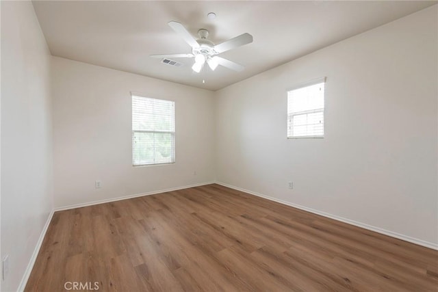 empty room with visible vents, ceiling fan, baseboards, and wood finished floors