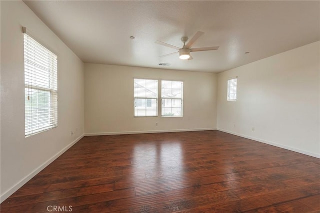 spare room featuring a healthy amount of sunlight, a ceiling fan, visible vents, and dark wood-style flooring