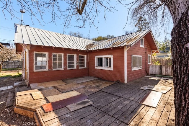 back of house featuring metal roof, a standing seam roof, and fence