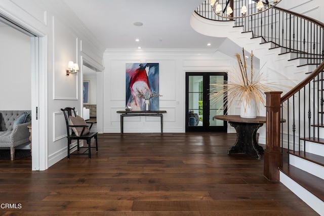 foyer with crown molding, dark wood finished floors, a decorative wall, stairway, and an inviting chandelier