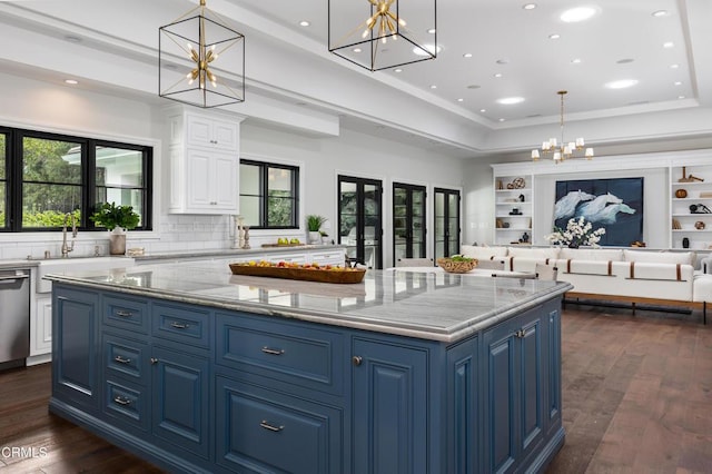 kitchen with a spacious island, open floor plan, decorative light fixtures, light stone countertops, and white cabinetry