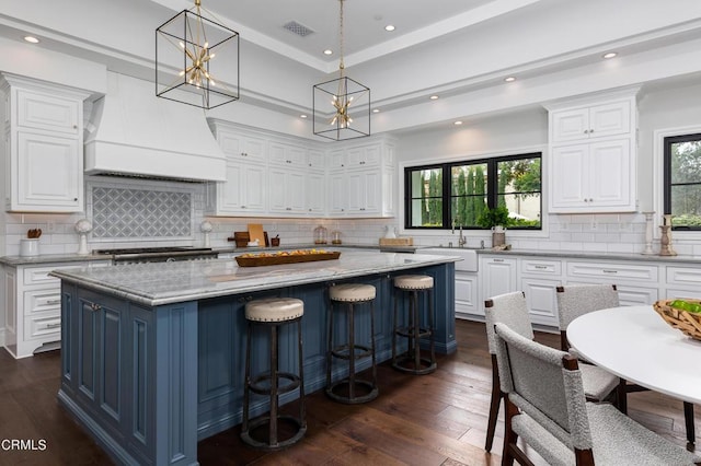 kitchen featuring a center island, pendant lighting, premium range hood, and white cabinetry