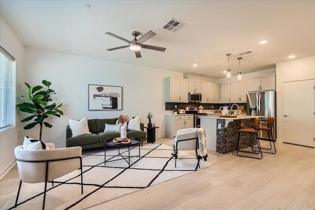 living area with light wood finished floors, a ceiling fan, visible vents, and recessed lighting