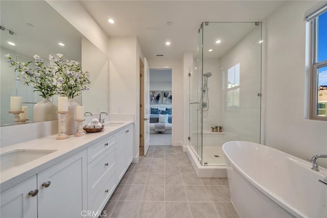 ensuite bathroom with double vanity, a freestanding tub, a sink, and tile patterned floors