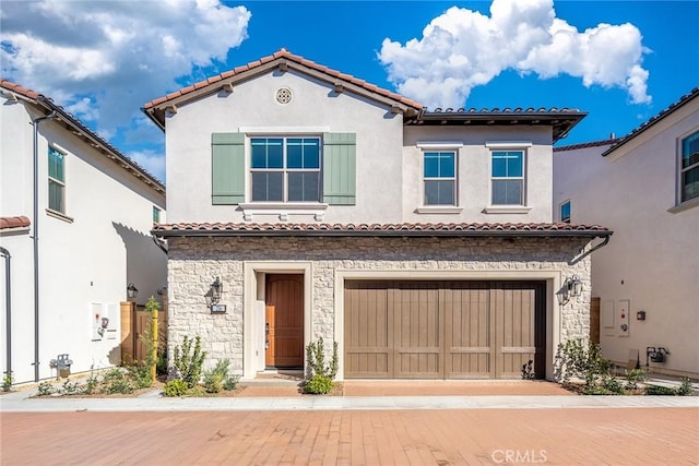 mediterranean / spanish home featuring stone siding, a tile roof, decorative driveway, and stucco siding