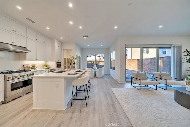 kitchen with a breakfast bar area, stainless steel stove, under cabinet range hood, light countertops, and a center island with sink