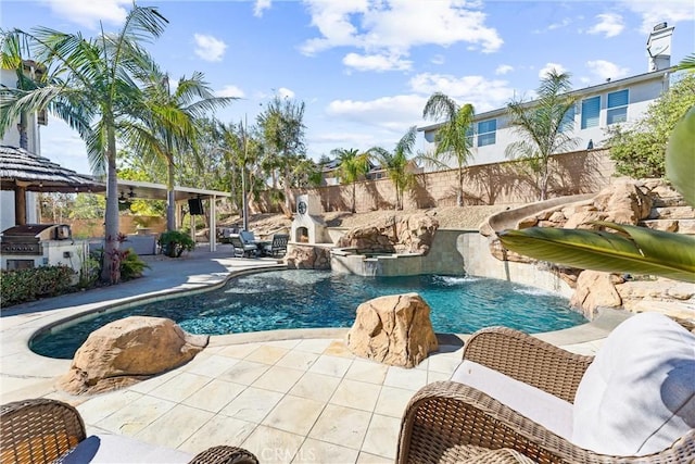 view of pool featuring a pool with connected hot tub, grilling area, an outdoor kitchen, a patio area, and fence