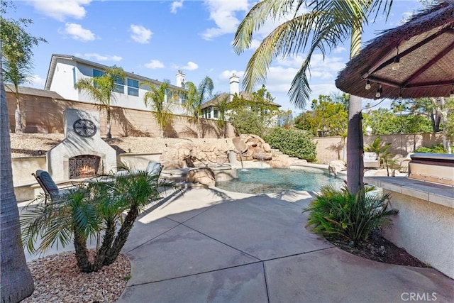 view of patio / terrace with a warm lit fireplace, a fenced backyard, and a fenced in pool