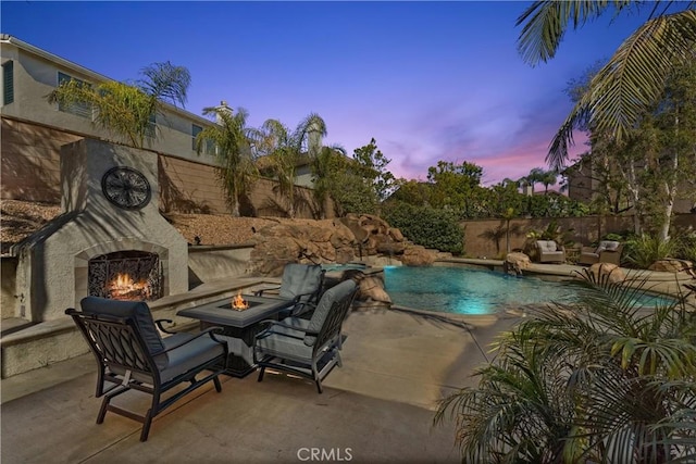 pool at dusk with a fenced in pool, a fenced backyard, a patio, and an outdoor living space with a fireplace