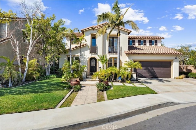 mediterranean / spanish home featuring an attached garage, a balcony, concrete driveway, stucco siding, and a front yard