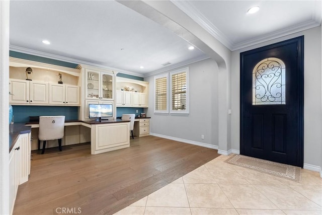 entryway featuring arched walkways, light wood-style flooring, ornamental molding, built in study area, and baseboards