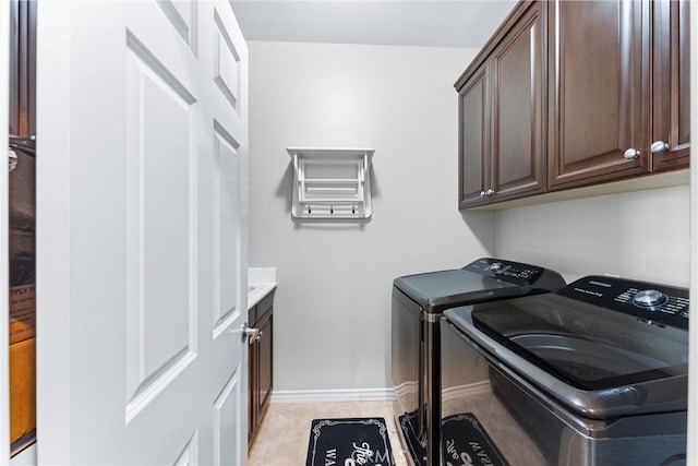 washroom featuring washing machine and clothes dryer, cabinet space, and baseboards