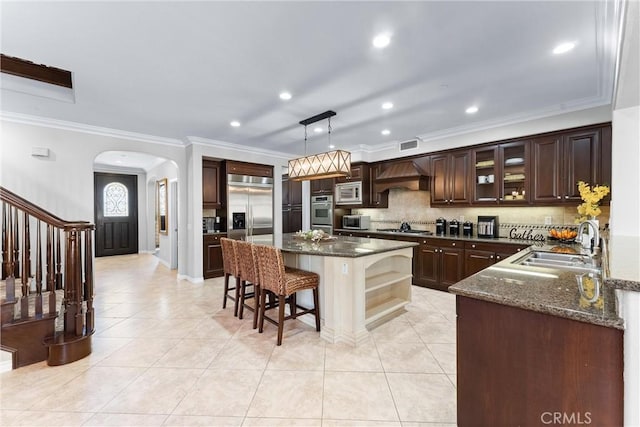 kitchen with arched walkways, a kitchen breakfast bar, a center island, built in appliances, and premium range hood