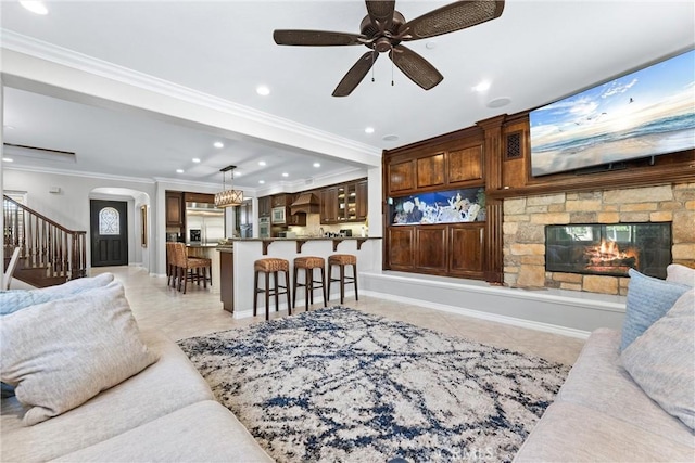 living room featuring arched walkways, a stone fireplace, light tile patterned flooring, stairway, and crown molding