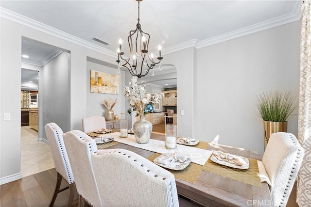 dining area with arched walkways, a notable chandelier, wood finished floors, visible vents, and crown molding