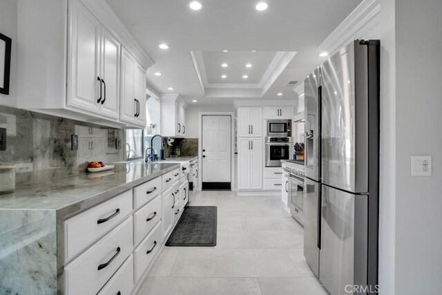 kitchen featuring appliances with stainless steel finishes, light stone counters, a tray ceiling, crown molding, and white cabinetry