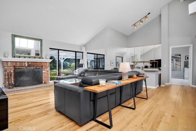 living room with high vaulted ceiling, baseboards, light wood-type flooring, a brick fireplace, and track lighting