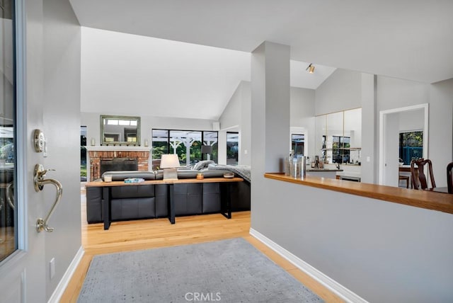 living area featuring vaulted ceiling, a fireplace, baseboards, and light wood-style floors