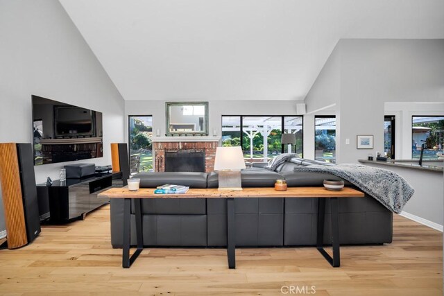 living area with high vaulted ceiling, a brick fireplace, and light wood finished floors