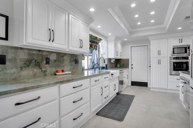 kitchen with appliances with stainless steel finishes, a raised ceiling, light stone countertops, and white cabinets