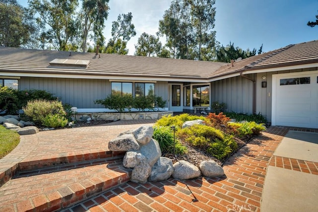 view of front of home with a garage, board and batten siding, and a tile roof