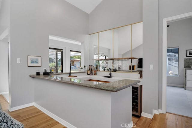 kitchen with a peninsula, high vaulted ceiling, a sink, and white cabinetry