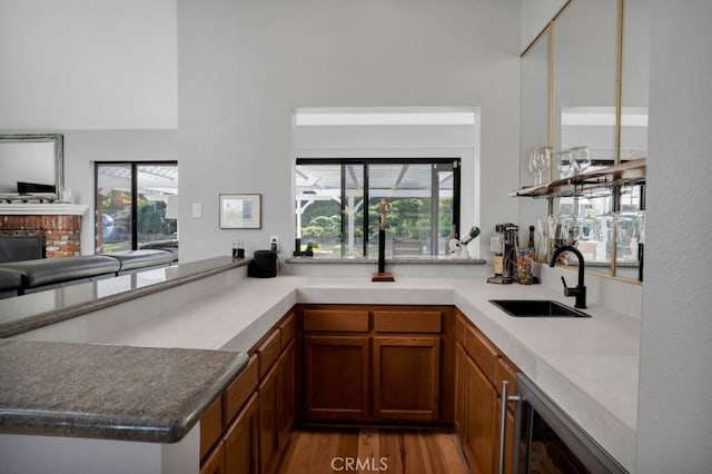 kitchen featuring brown cabinetry, wine cooler, a peninsula, a sink, and a wealth of natural light