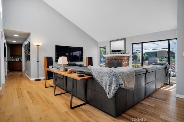 living room with light wood-style floors, baseboards, a fireplace, and high vaulted ceiling