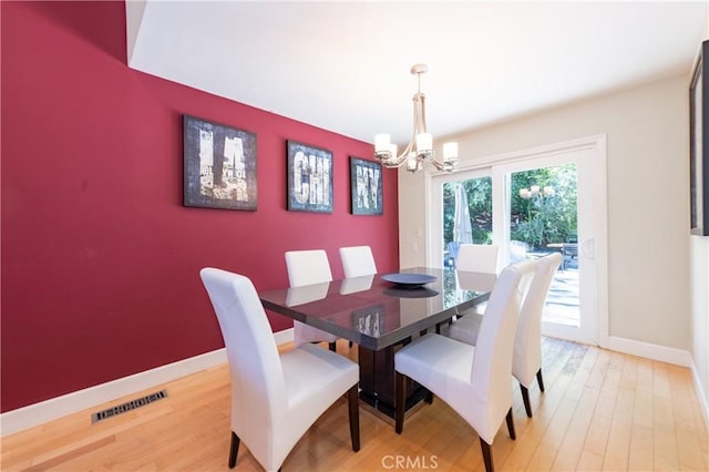 dining area with baseboards, visible vents, an accent wall, wood finished floors, and a chandelier