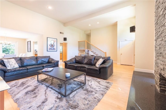 living room with stairway, light wood-style floors, a stone fireplace, a chandelier, and baseboards