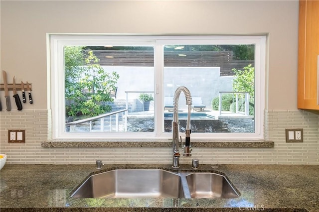 kitchen featuring tasteful backsplash, dark stone countertops, and a sink