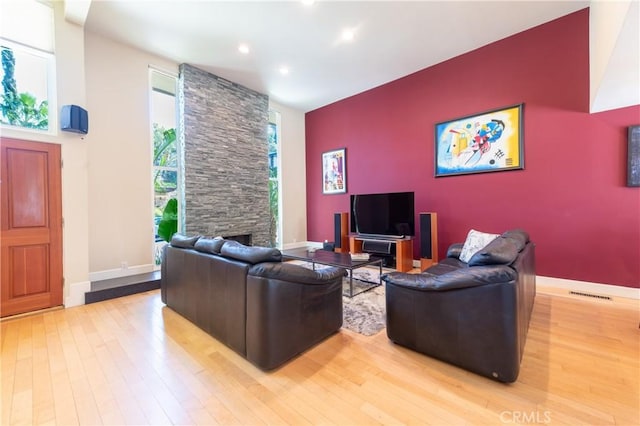 living area featuring light wood-style floors, visible vents, baseboards, and a stone fireplace