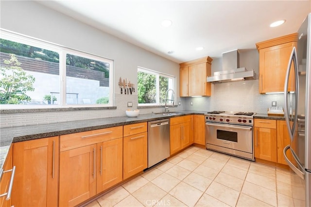 kitchen featuring dark stone countertops, a sink, stainless steel appliances, wall chimney range hood, and backsplash